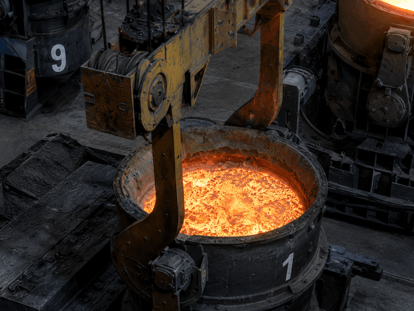 A ladle crane hook descending onto ladle 1, its molten bath open — the engagement.